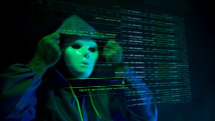 Anonymous hacker wearing a mask and hoodie interacting with digital data in a dark room