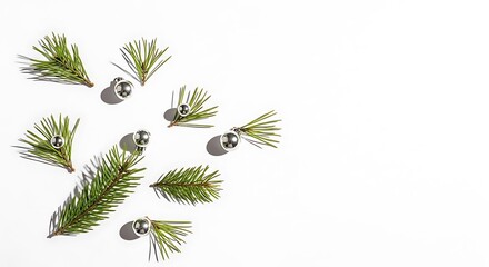 A minimalist arrangement of pine sprigs and small silver bells scattered on a white background, evoking a festive holiday theme.