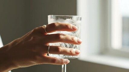 Close up of a hand holding a glass of water with ice cubes.