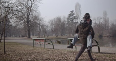 A happy young couple enjoying a romantic and playful piggyback ride through a beautiful park. They share moments of joy and affection by the serene lake, celebrating their love and togetherness. - Powered by Adobe