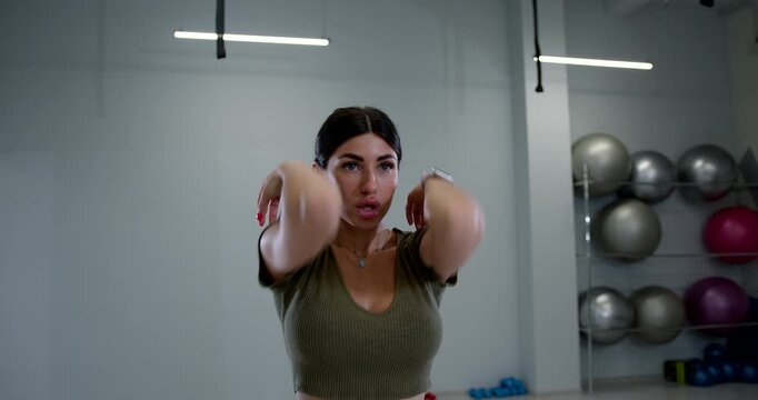 athletic woman is actively engaging in shoulder rotations to improve her flexibility and strength in a modern gym environment. The space features various workout equipment.