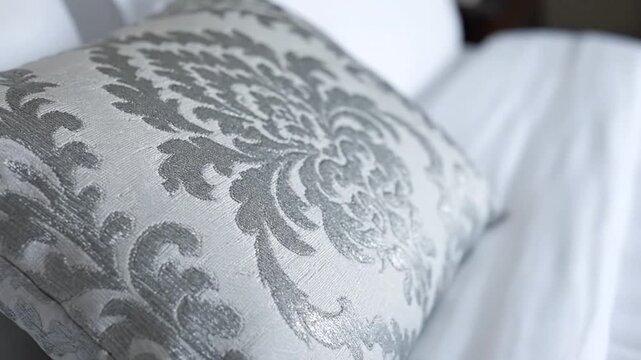 Close-up of a decorative pillow with a damask pattern on a bed with white linens.