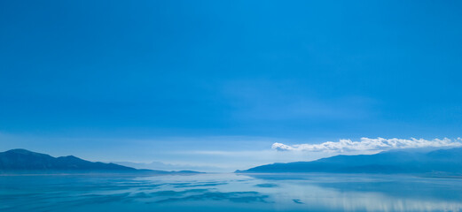 An expansive aerial shot capturing the deep blue surface of a massive lake meeting the horizon with hazy mountains in the distance creating a sense of freedom and endless natural space