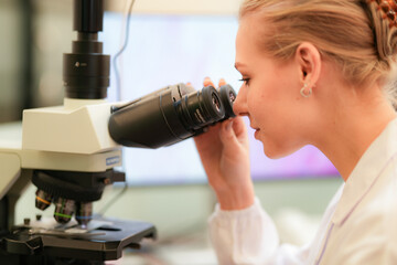A medical lab technician prepares a tissue sample for a biopsy test. She is using a microscope to study the cells and help doctors with a patient's diagnosis.
