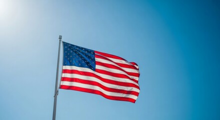 Fototapeta premium The patriotic symbol of the United States of America, the flag, waving gracefully in the wind against a bright sunlit blue sky