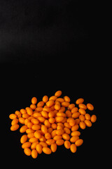 A pile of orange pills on a black background. The pills are small and round, and they are scattered across the surface of the black background. Concept of organization and order.