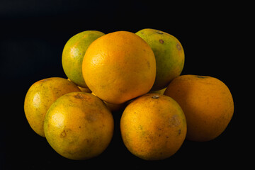 A bunch of oranges are piled on top of each other. The oranges are all different sizes and are all in the same color.