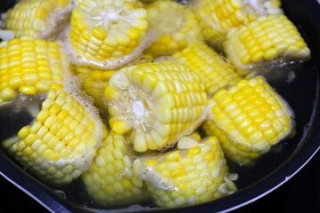 Corn pieces boiling in hot water inside a pan.