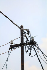 Messy and tangled electrical wires on an old utility pole against a pale blue sky. Symbolizing complexity, connection, and urban infrastructure