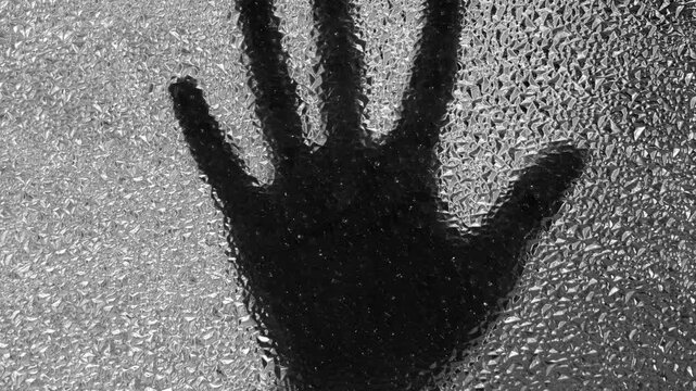 Silhouette of hand touching window. Black and white.