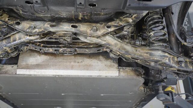 Slow right to left tracking shot showing results after applying lanolin rust protection to underside of electric vehicle