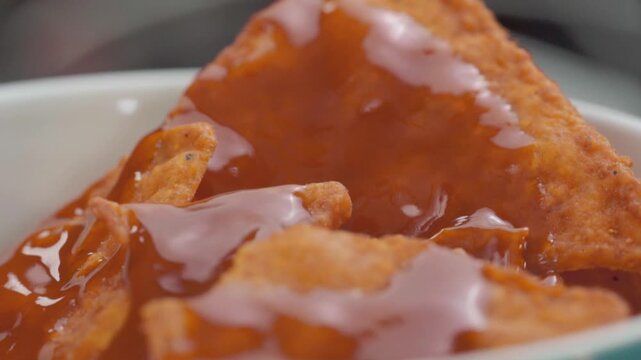 Adding spicy red sauce to nachos while the plate rotates. Close-up