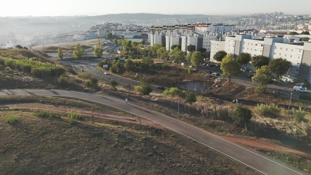 Drone aerial above Parque das Artes e do Desporto in Amadora, Portugal showing a runner, the park&rsquo;s greenery, and surrounding urban buildings.
