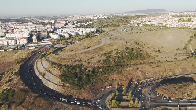 Drone aerial over Amadora, Portugal showing city traffic, Av. Eduardo Malta, and Parque das Artes e do Desporto surrounded by urban scenery.