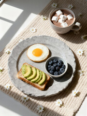 A healthy and delicious breakfast featuring avocado toast, a sunny-side-up egg, fresh blueberries, and hot chocolate with marshmallows in bright sunlight.