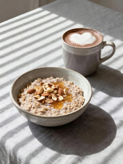 A cozy morning breakfast featuring a bowl of warm oatmeal topped with almonds and honey, served with a mug of hot chocolate with heart art.