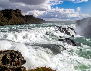 Large waterfall cascades over rocks beneath a cloudy sky