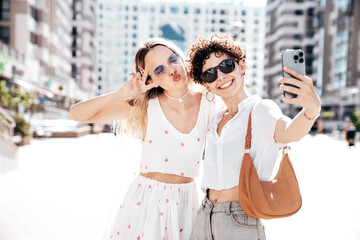 Two young beautiful smiling hipster female in trendy summer white t-shirt and shorts clothes. Sexy...