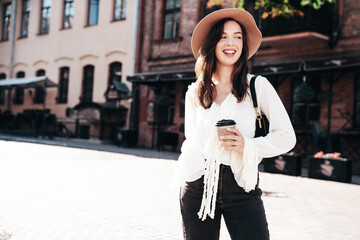 Lifestyle portrait of young stylish woman dressed in white blouse. Model walking with coffee cup in...