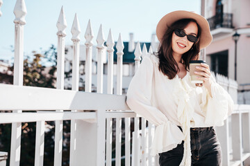 Lifestyle portrait of young stylish woman dressed in white blouse. Model walking with coffee cup in...