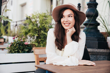 Portrait of beautiful young woman 
in hat. Model at coffee shop. Female outdoors in sunny day. In...