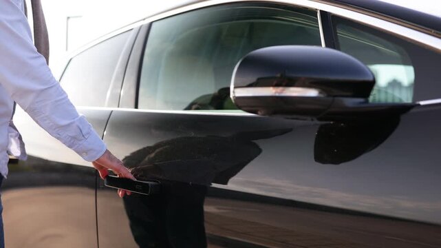 A man's hand reaching for the door handle of a sleek, black car, ready to open it.