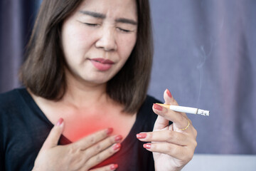 Asian woman touching her chest in pain after smoking a cigarette, showing signs of heart or lung...