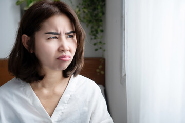 Asian woman with unhappy, angry expression, showing mood swings and irritation caused by PMS or...