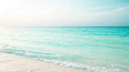 Obraz premium Gentle waves lap against a soft sandy shore as the sun rises over a tranquil beach. The clear turquoise water sparkles under the morning light, creating a peaceful atmosphere