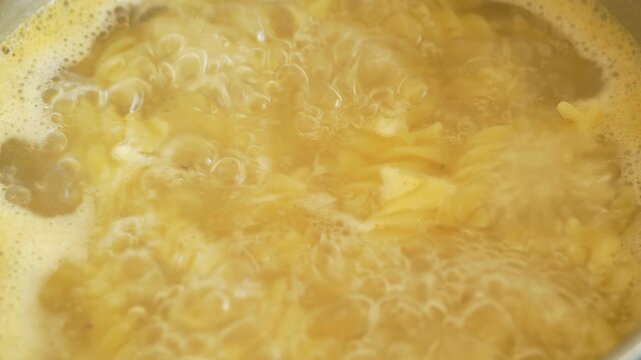 Cooking pasta in pot of boiling water on stove in kitchen. Italian Pasta. Macaroni of various varieties in very hot voda