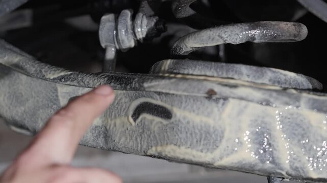 Man uses finger to show lanolin rust protection product freshly applied to car underside, close up.