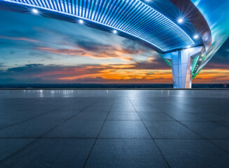 Empty square floor and modern bridge building with city skyline at sunset