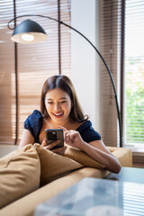 Happy young asian woman checking social media holding smartphone at home. Smiling young  woman...