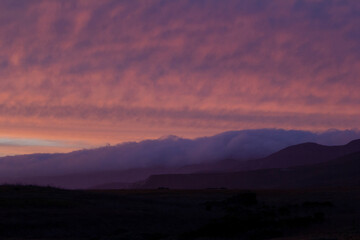Soft pastel clouds over shadowy rolling hills at sunset, landscape