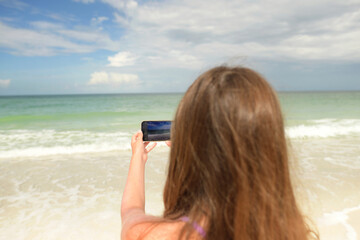 Behind young girl using cell phone to take picture of tropical b