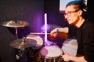 Young musician practicing drumming in a studio with colorful lights