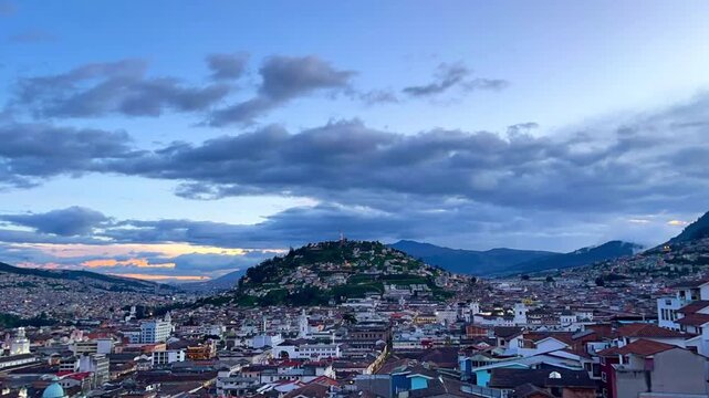 Quito, Ecuador's capital city, is sprawling under a cloudy sky with El Panecillo hill standing out in the background, creating a picturesque cityscape at sunset