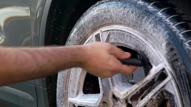 Close up cleaning sports car wheels with snow foam and black red wheel barrel brush