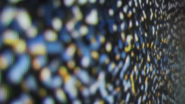 Macro shot of an abstract background with blurry, flickering digital noise. Colorful blue, white, and yellow bokeh dots move vertically on a screen, creating a technological texture.