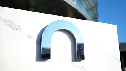 Sleek metallic arch design on a luxurious white marble base showcasing reflections of modern architecture and a clear blue sky Contemporary urban exterior detail - Powered by Adobe