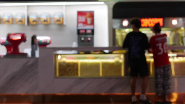 Blurred cinema concession stand with customers buying popcorn and drinks under colorful neon lighting at movie theater