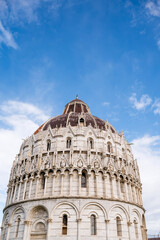 Fototapeta premium Ornate Gothic dome of Pisa Baptistery with white marble arcades, pointed arches, decorative spires and weathered copper cupola against blue sky in Tuscany Italy