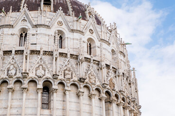 Ornate Gothic dome of Pisa Baptistery with white marble arcades, pointed arches, decorative spires and weathered copper cupola against blue sky in Tuscany Italy