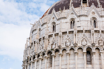 Fototapeta premium Ornate Gothic dome of Pisa Baptistery with white marble arcades, pointed arches, decorative spires and weathered copper cupola against blue sky in Tuscany Italy