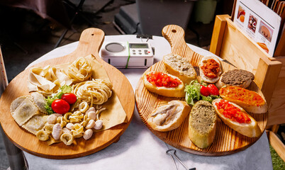 Double Italian Appetizer Spread: Fresh Uncooked Pasta Varieties and Assorted Crostini with Tomato, Olive Spread, and Anchovy on Rustic Round Wooden Boards