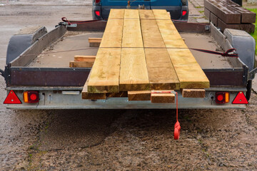 Transportation of wooden boards on a car trailer for construction work
Wooden planks securely loaded on a flatbed trailer attached to a car. Lumber delivery for building, carpentry