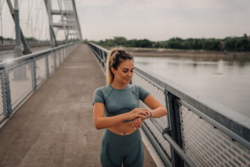 Young sporty woman checking smartwatch on bridge during workout