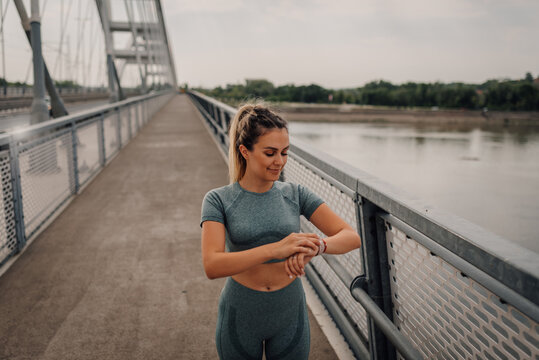 Young sporty woman checking smartwatch on bridge during workout