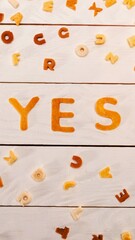 Orange alphabet letters spell yes on white wooden surface