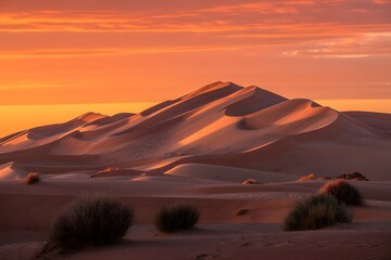 Majestic desert dunes sculpted by wind under a vibrant orange and yellow sunset sky creating dramatic shadows and highlights